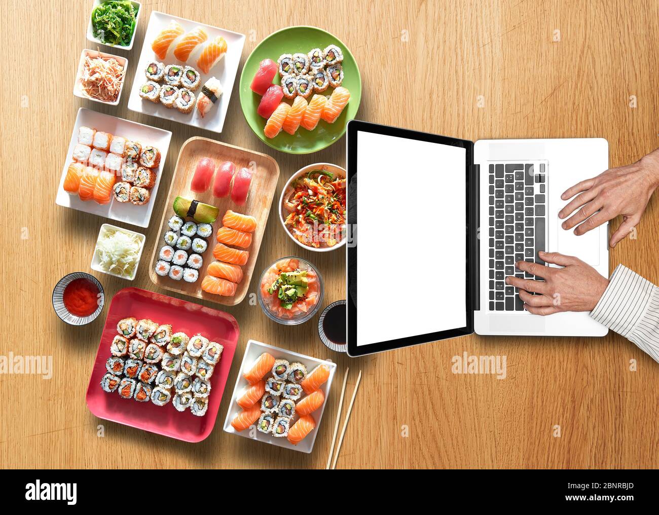 Hombre de negocios trabajando en su ordenador portátil sobre mesa de madera con surtido de bandejas y plato de sushi y maki Foto de stock