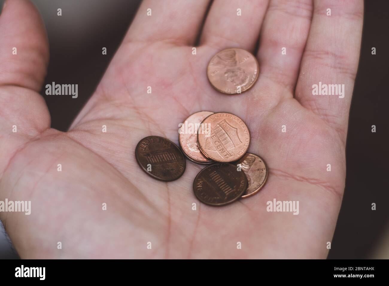 Las personas tienen a mano un puñado de centavos de Estados Unidos de América (EE.UU.), una moneda inútil sobre un fondo marrón. Cambio de moneda. Foto de stock