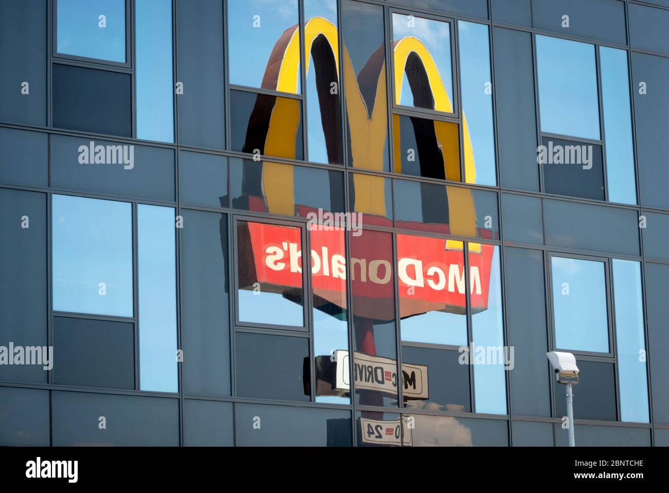 El logotipo y el cartel de McDonald's reflejan el edificio de cristal como una composición inusual y única Foto de stock