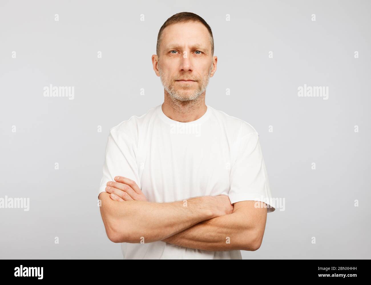 Hombre en camiseta blanca con los brazos cruzados sobre fondo blanco. Foto de stock