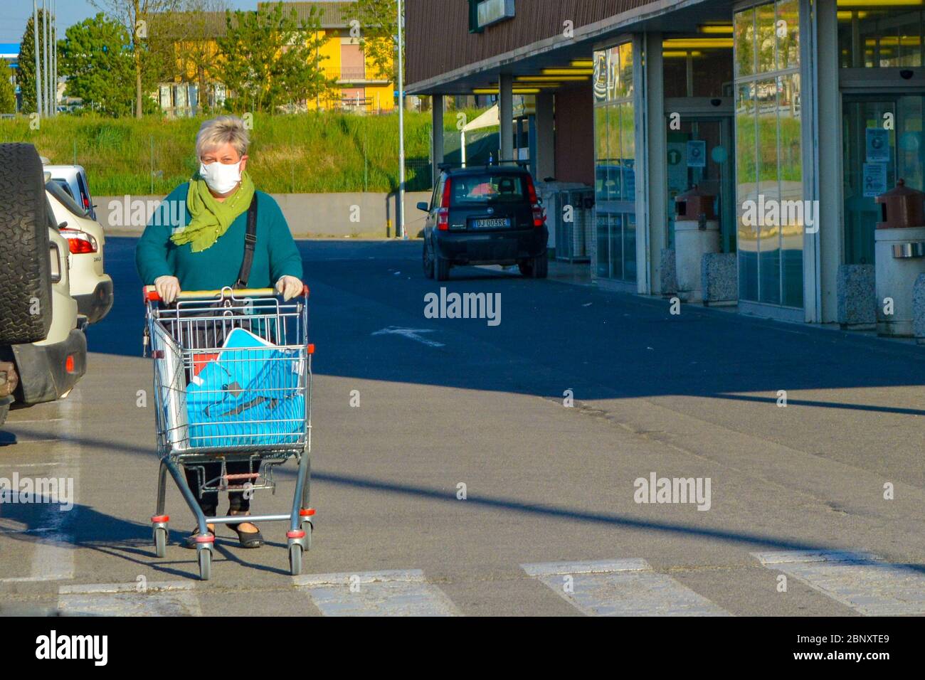 Mujer italiana de edad, pensionista con máscara facial coronavirus empujando su carrito de compras fuera de una tienda de comestibles. Lady teme por la pandemia de COVID-19. Foto de stock