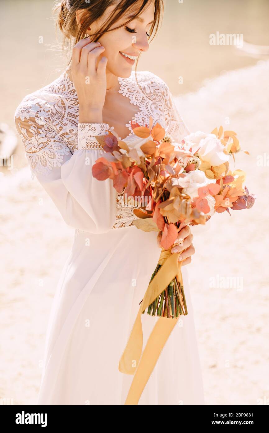 Hermosa novia en un vestido blanco con mangas y encaje, con un ramo de otoño amarillo de flores secas y rosas de peony, en el Lago di Braies en Italia Fotografía de Hermosa novia en un vestido blanco con mangas y encaje, con un ramo de otoño amarillo de flores secas y rosas de peony, en el Lago di Braies en Italia Fotografía de