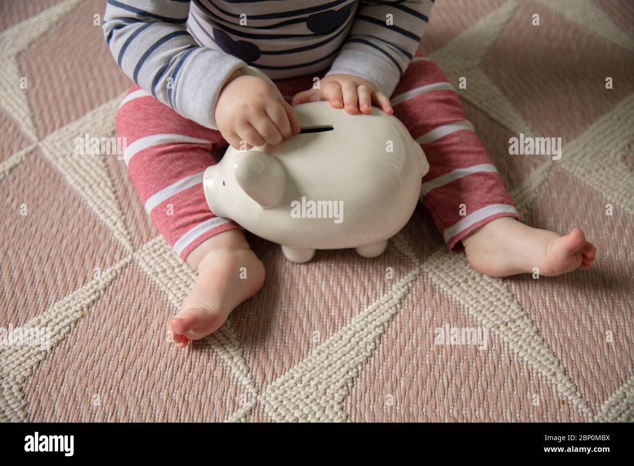 Un bebé pone dinero en un banco de piggy ahorrando para su futuro Foto de stock