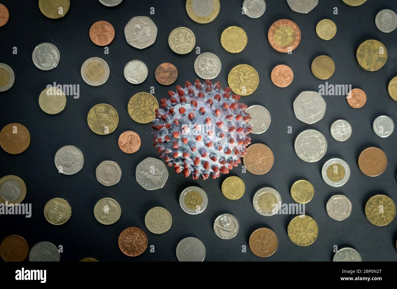 Vista superior de una bola pintada como un virión SARS-CoV-2 en medio de muchas monedas de diferentes países Foto de stock