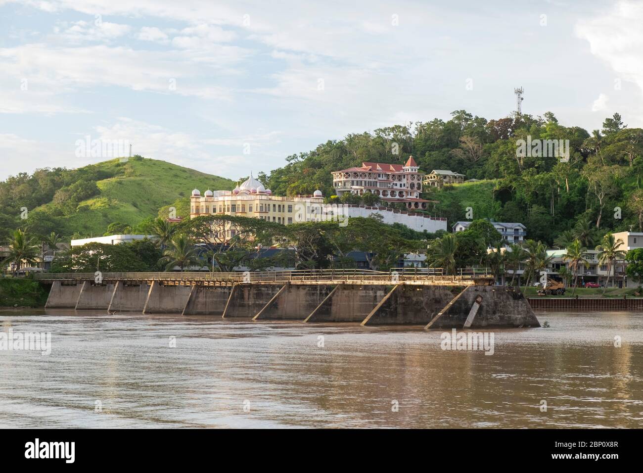 Vista a través del río Sigatoka hacia el puente ferroviario dañado y el templo en la ladera de Singatoka, Fiji. Foto de stock