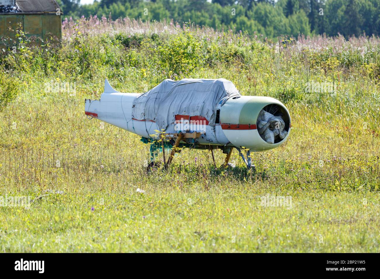 Un viejo avión sin alas, cubierto con un tarp, se encuentra en un prado en un día soleado de verano Foto de stock