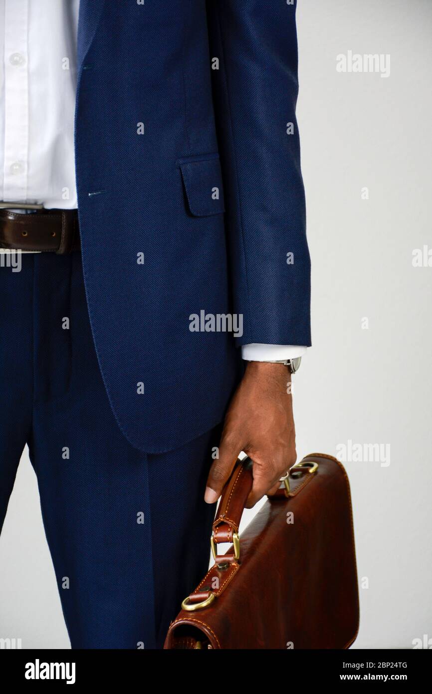 Primer plano de un joven hombre de negocios de piel oscura en azul formal llevar portando maletín. Traje de negocios. Vista delantera, sección media. Foto de stock