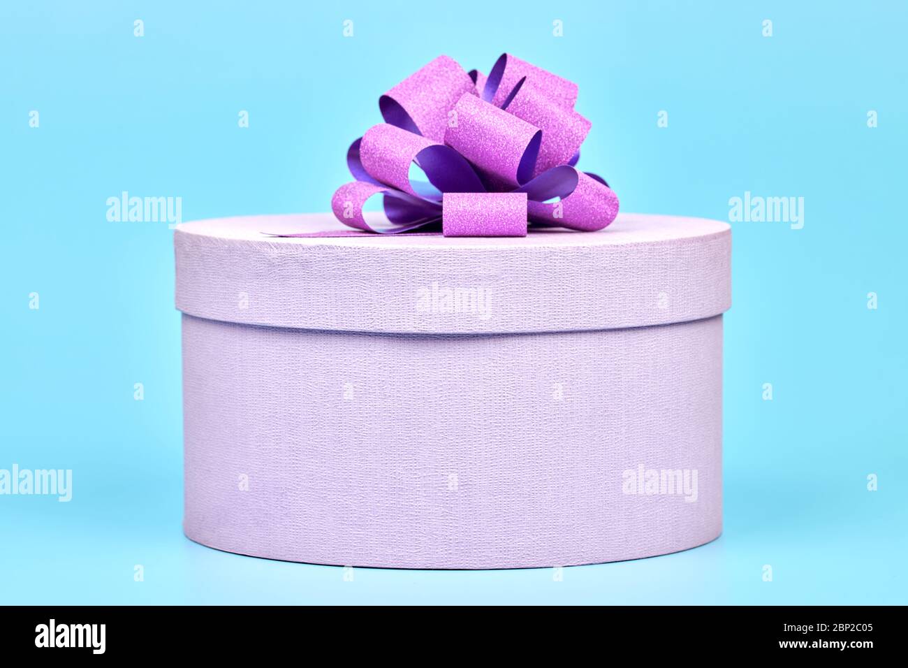 Caja de regalo redonda con lazo. Caja cerrada púrpura para regalo sobre  fondo azul. Paquete sorpresa para cualquier día de fiesta: Cumpleaños, San  Valentín, Navidad, un Fotografía de stock - Alamy