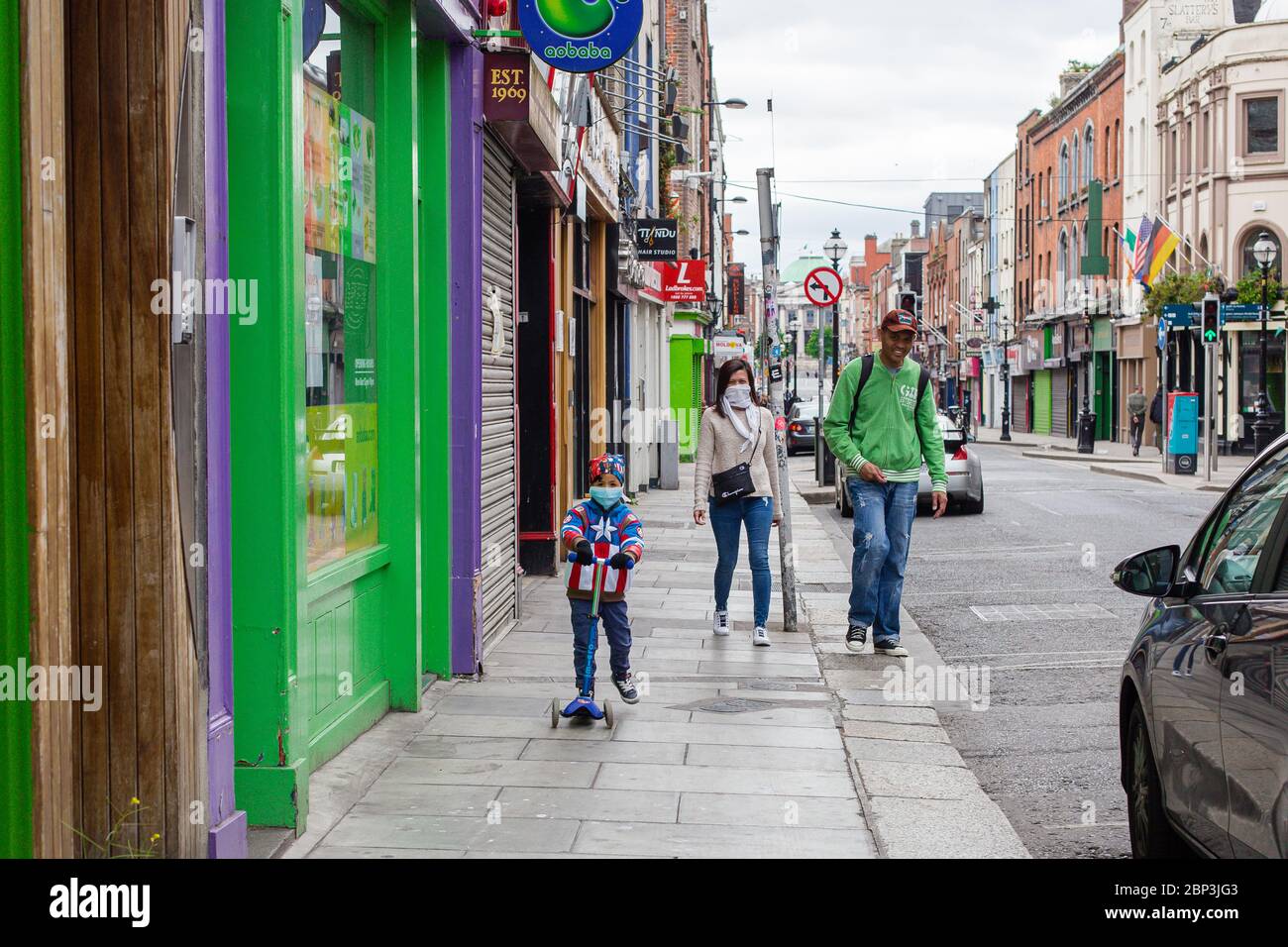 Niño en una scooter con una chaqueta superhéroe y máscara protectora vista panorámica con sus padres en el centro de la ciudad de Dublín durante la pandemia de covid-19 Foto de stock