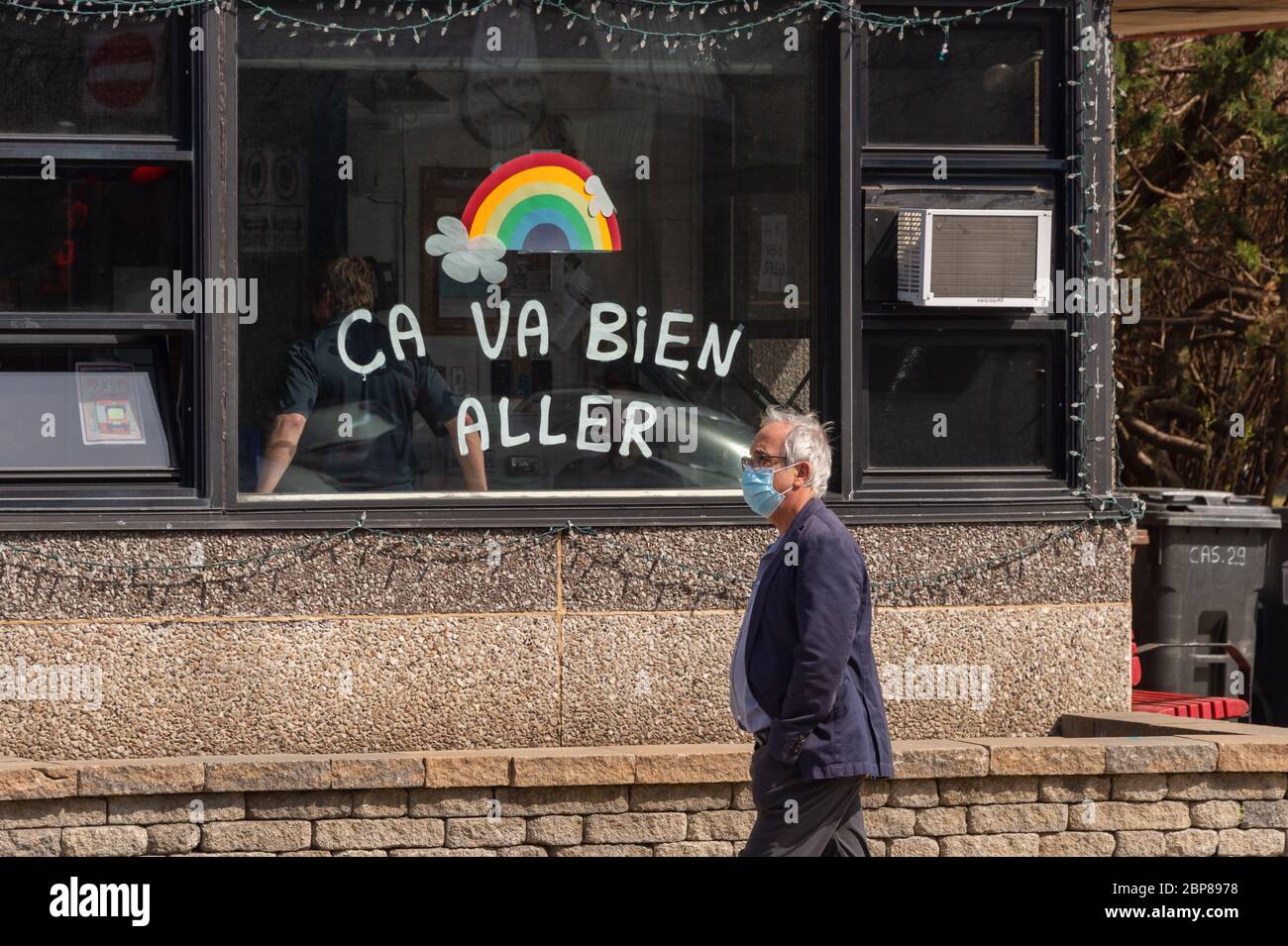 Montreal, CA - 17 de mayo de 2020: Hombre con máscara para la protección contra COVID-19 caminando frente al arco iris dibujando en la calle Masson. Foto de stock