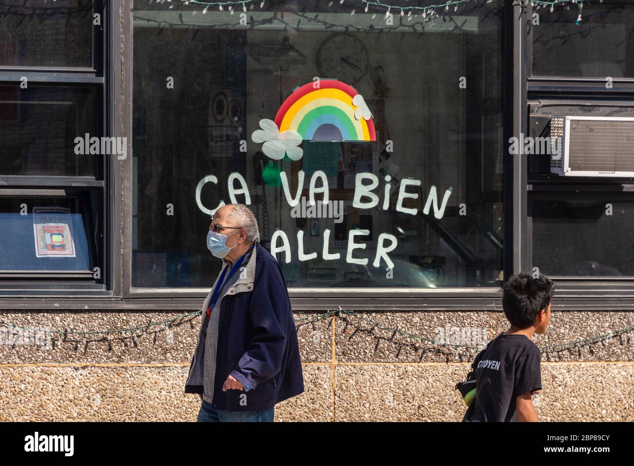 Montreal, CA - 17 de mayo de 2020: Hombre maduro con máscara facial para la protección contra COVID-19 caminando frente al arco iris dibujando en la calle Masson. Foto de stock