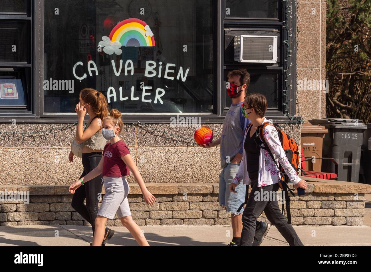 Montreal, CA - 17 de mayo de 2020: Familia con máscaras para la protección contra COVID-19 caminando frente al arco iris dibujando en la calle Masson. Foto de stock