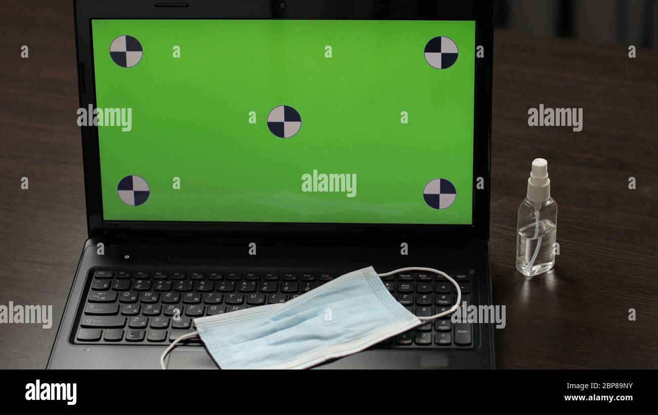 Máscara médica en un teclado de ordenador portátil con una pantalla verde,  tecla de croma. Desinfectante o jabón líquido cerca del portátil. Trabajo a  distancia en cuarentena de coronavirus covid-19. Quédate en