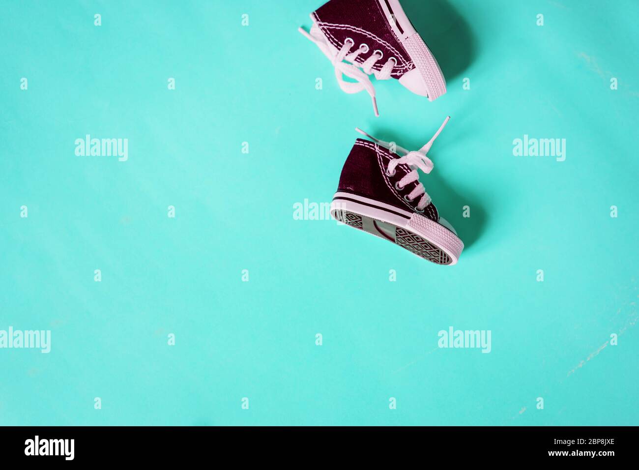 Vista superior de zapatos bebé granate aislados sobre fondo color menta. Zapatillas de lona en miniatura. Copiar espacio para el texto o diseño, plano. Concepto de zapatería Fotografía de stock -