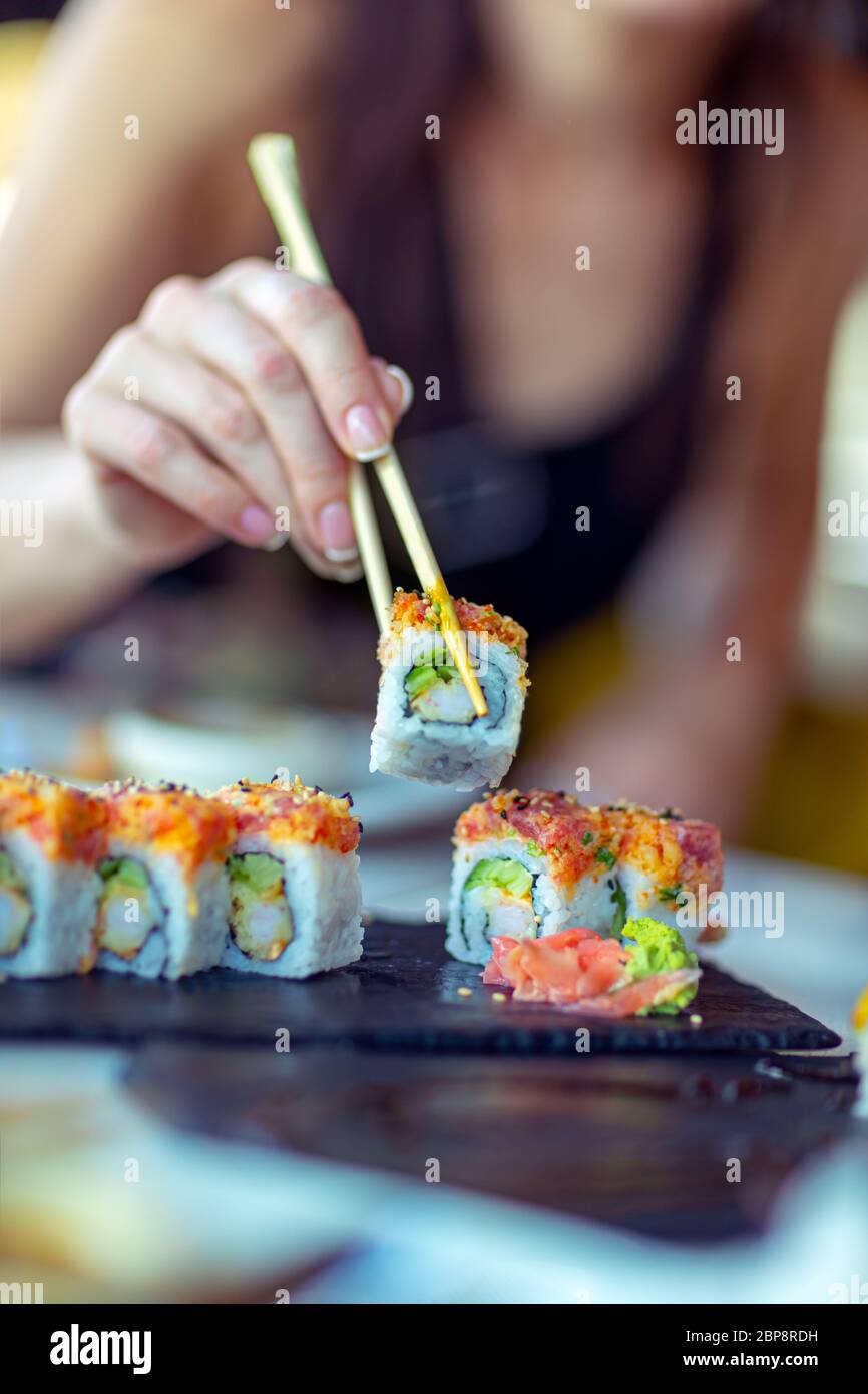 Comer en el restaurante de sushi, una mujer con un manicure perfecto usando palillos  chinos toma un pedazo de rollo, disfrutar de alimentos sanos y sabrosos, un  tradicional Fotografía de stock -