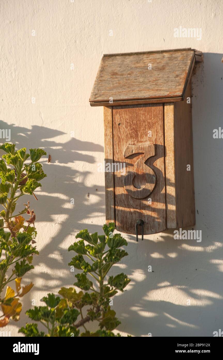 Antiguo postbox de madera #3 montado en una pared, a la sombra de las plantas. El número 3 está grabado en la puerta. SADOWS le da un aire de misterio Foto de stock