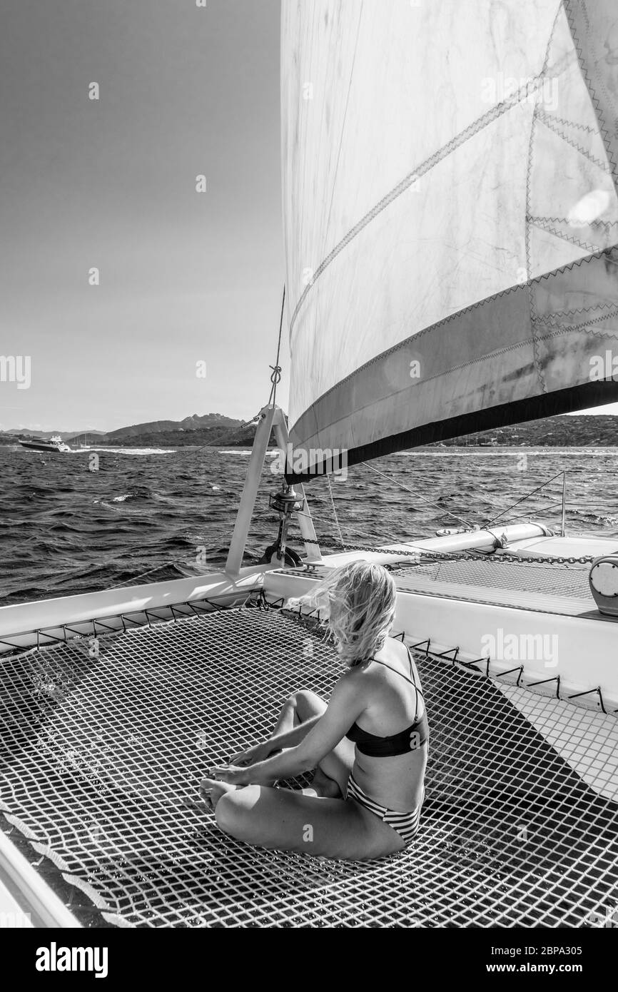 Bella mujer en un relajante crucero de verano, sentarse y tomar el sol en una hamaca de lujo en catamarán alrededor del archipiélago Maddalena, Sardi Foto de stock