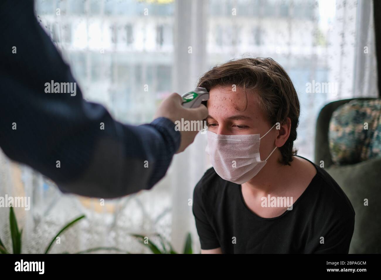 El padre está revisando la temperatura de su hijo con un termómetro infrarrojo en la casa Foto de stock