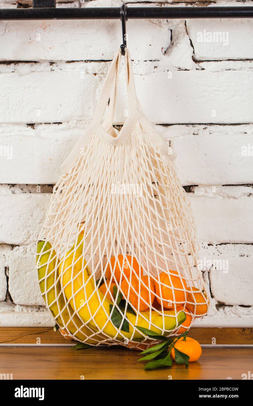 malla bolsa reutilizable con frutas enganchadas en pared de ladrillo blanco cero concepto de residuos Foto de stock