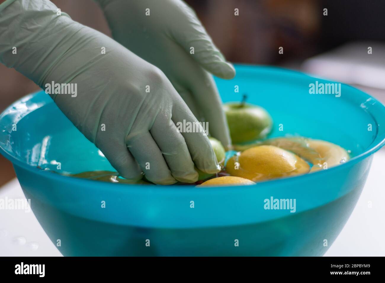 Lavar las frutas en un recipiente con guantes de plástico. Las frutas se colocan en el agua en un tazón verde para la limpieza después de las compras. Foto de stock