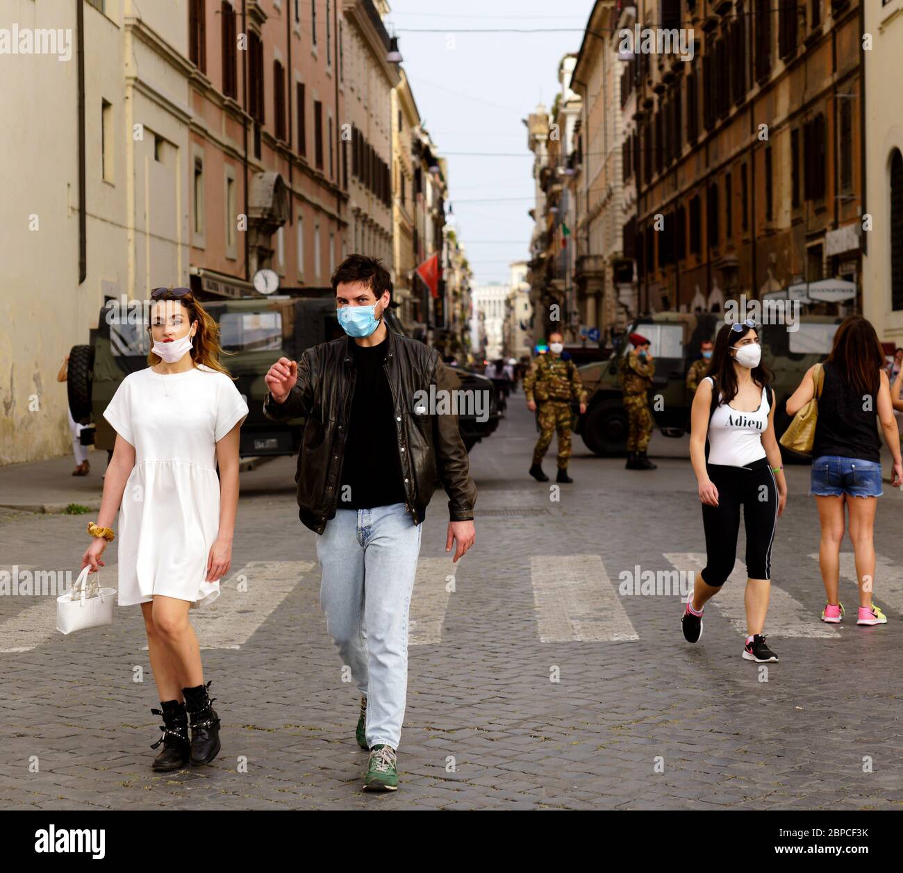 Pareja joven con máscaras médicas caminando en el centro de Roma durante la fase 1 del coronavirus Covid 19. Furgonetas del ejército con patrullas militares en el fondo. Italia, Europa, Unión Europea, UE. Foto de stock