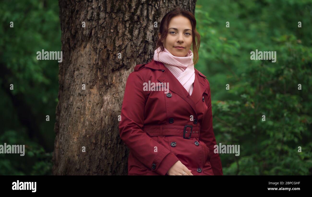 Retrato de una joven mujer bonita en chaqueta roja de pie cerca del árbol en el bosque de primavera. Foto de stock