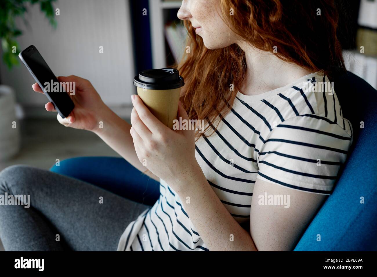 Mujer sentada con un teléfono y una taza de café Foto de stock