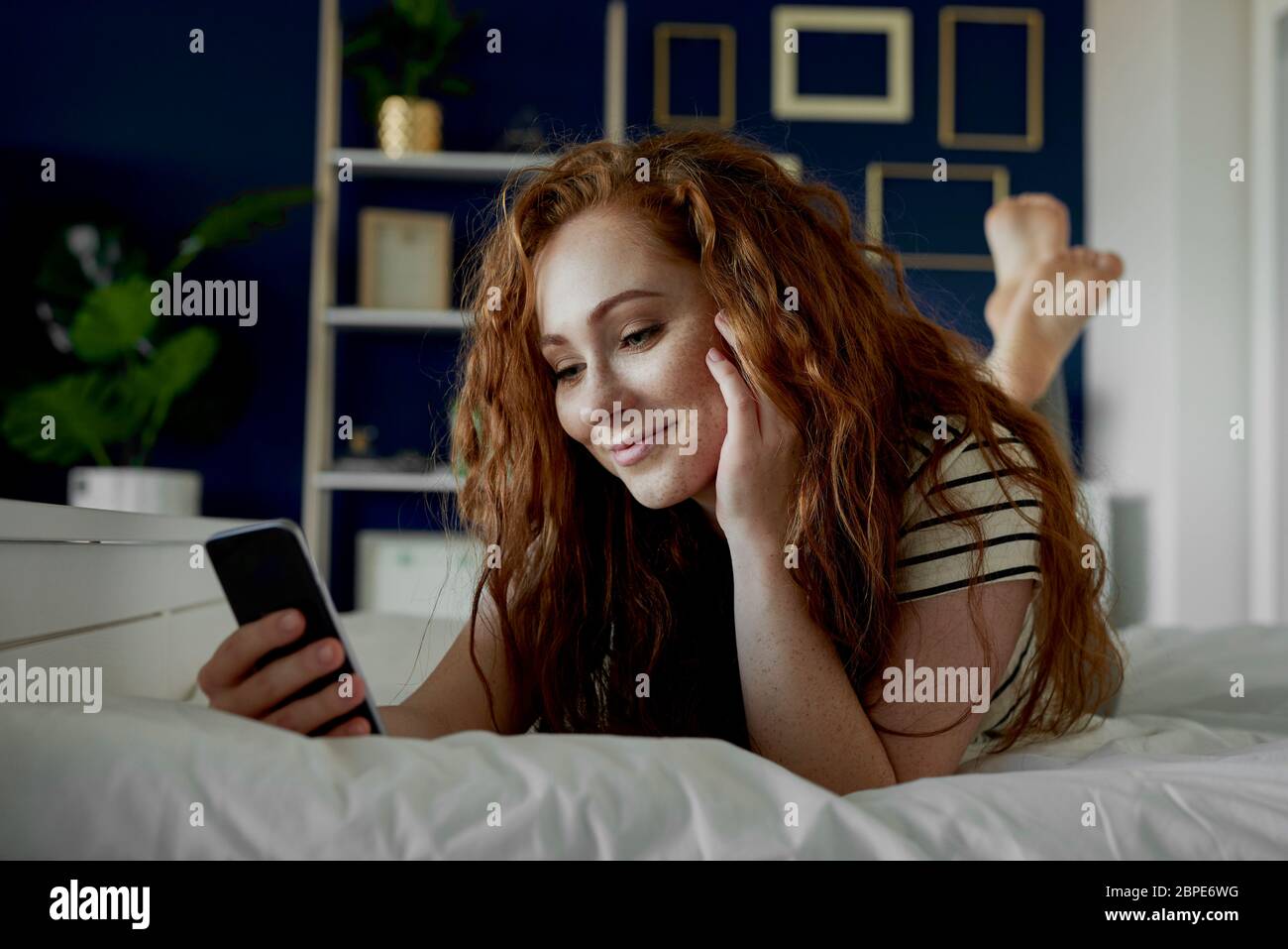 Mujer joven usando el teléfono mientras se está en la cama Foto de stock
