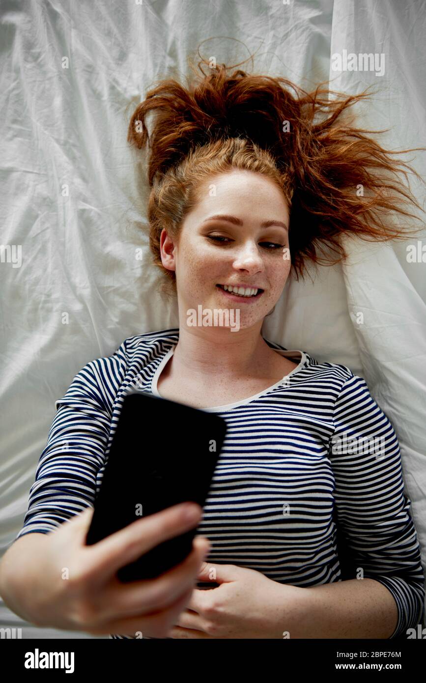 Vista superior de la mujer en la cama tomando un selfie Foto de stock