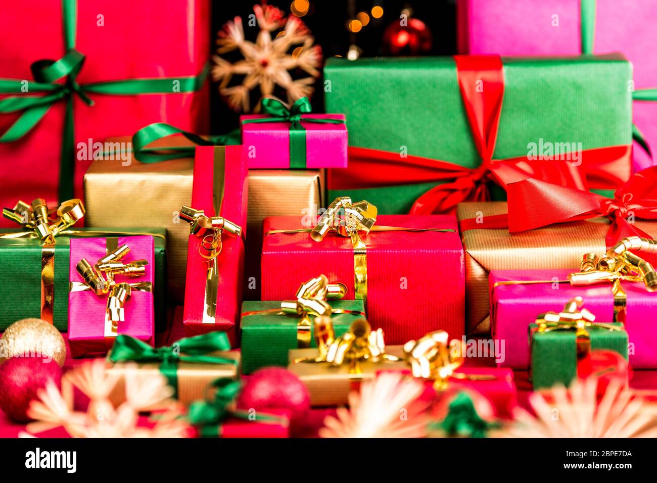 Multitud de regalos de Navidad esperando ser entregados. Envuelto en colores individuales. Rojo, verde, dorado y magenta. Bolas y estrellas borrosas en frente a Foto de stock