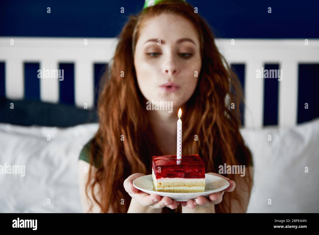 Mujer de la pelirroja soplando una vela de cumpleaños en el pastel Foto de stock