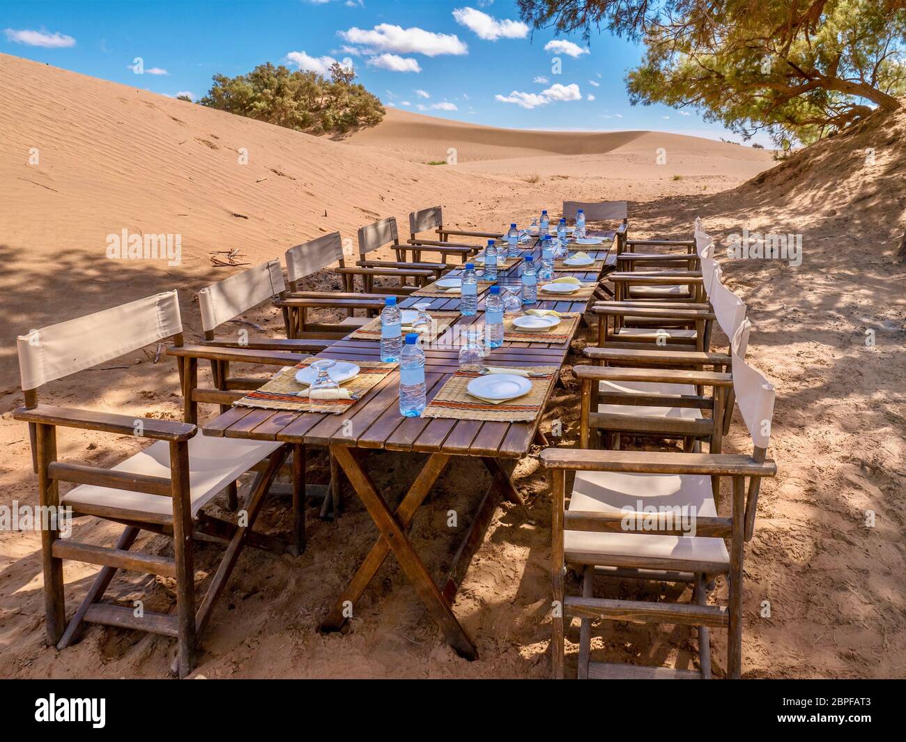 Una larga mesa de madera y sillas preparadas para un almuerzo turístico en el desierto del Sahara, Marruecos. Conceptual para las cancelaciones de último minuto de turistas y viajes Foto de stock