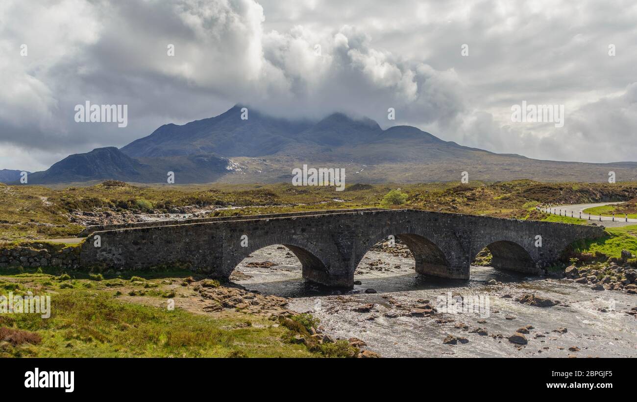 Antiguo puente de ladrillo de época cruzando el río en Sligachan, Isla de Skye, Escocia con ovejas en el puente y paisaje escocés, vegetación, colinas y mountaos Foto de stock
