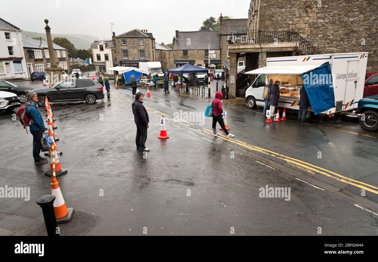 Settle, North Yorkshire, Reino Unido. 19 de mayo de 2020. Distanciamiento social como los compradores hacen cola en la lluvia en el mercado agotado del martes, se establecen, North Yorkshire. La mayoría de los puestos no alimentarios están ahora ausentes del mercado semanal, como resultado de las restricciones de Covid-19. Crédito: John Bentley/Alamy Live News Foto de stock