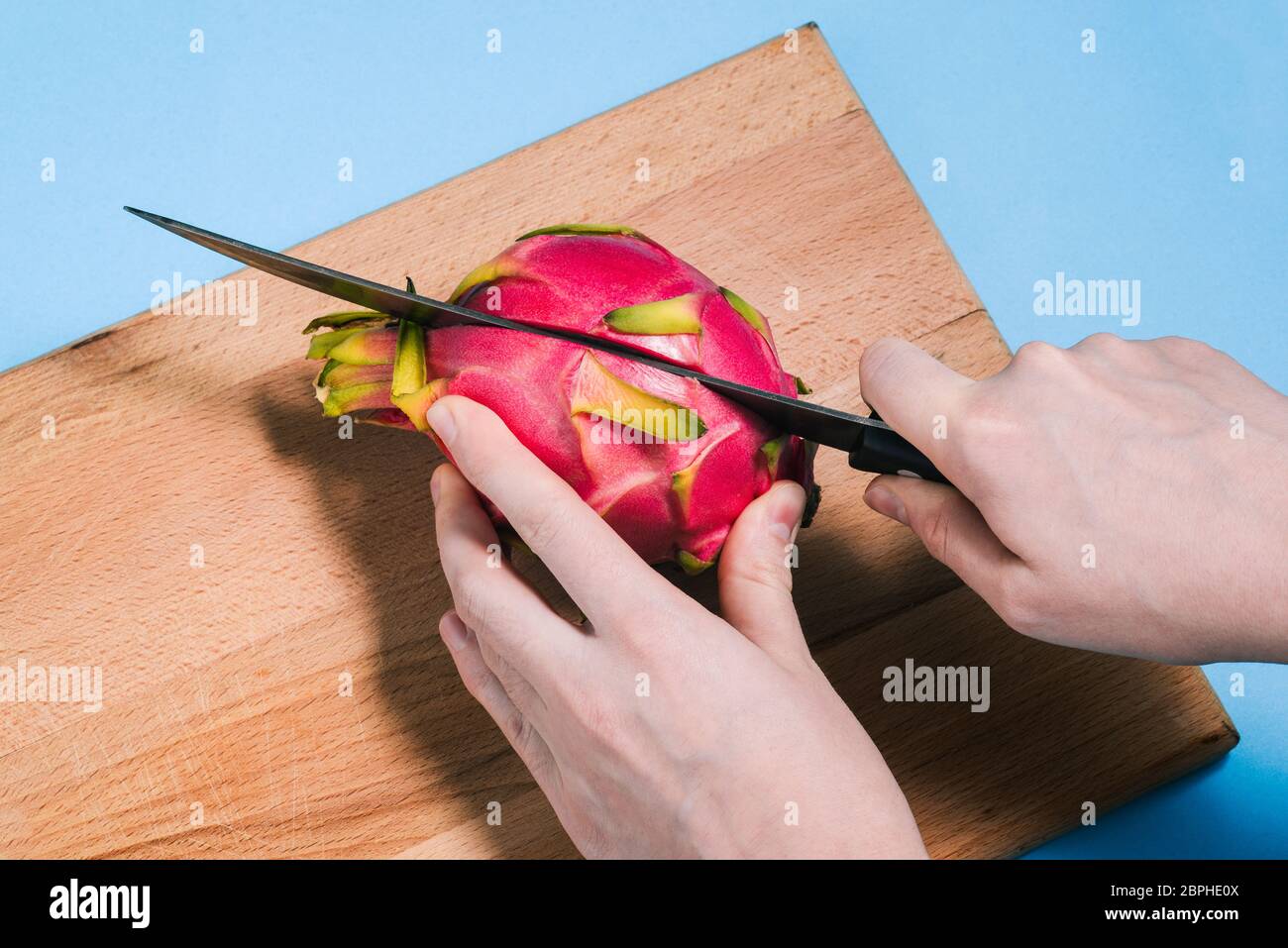 Primer plano de las manos de una mujer cortando una fruta madura de pitaya con un cuchillo en una tabla de madera. Pattaya está cortado en dos partes. La vista desde arriba. Foto de stock
