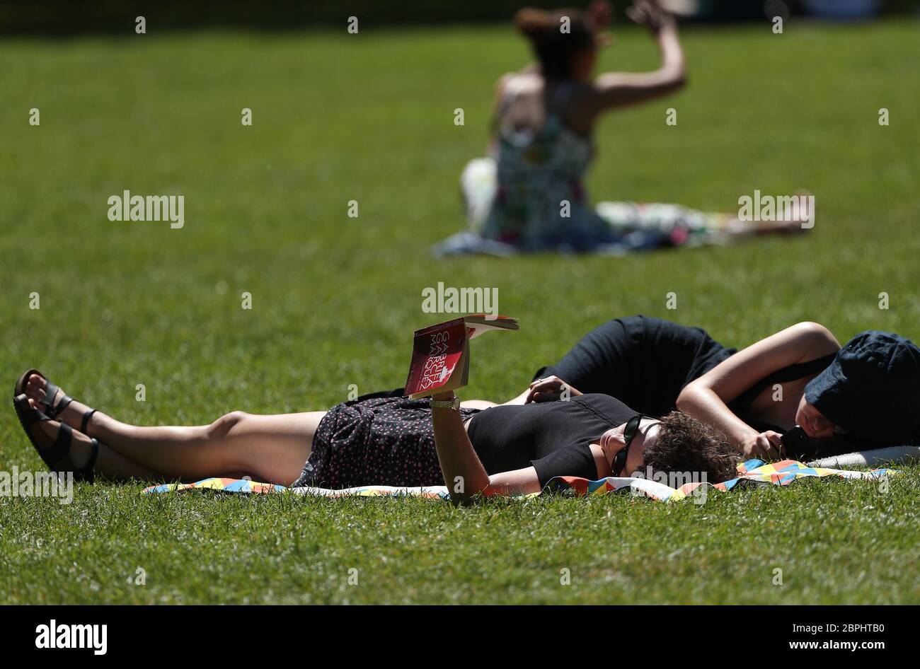 Una mujer leyendo un libro mientras toma el sol en el clima caluroso, en el parque London Fields, al este de Londres, después de la introducción de medidas para sacar al país de la encierro. Foto de stock