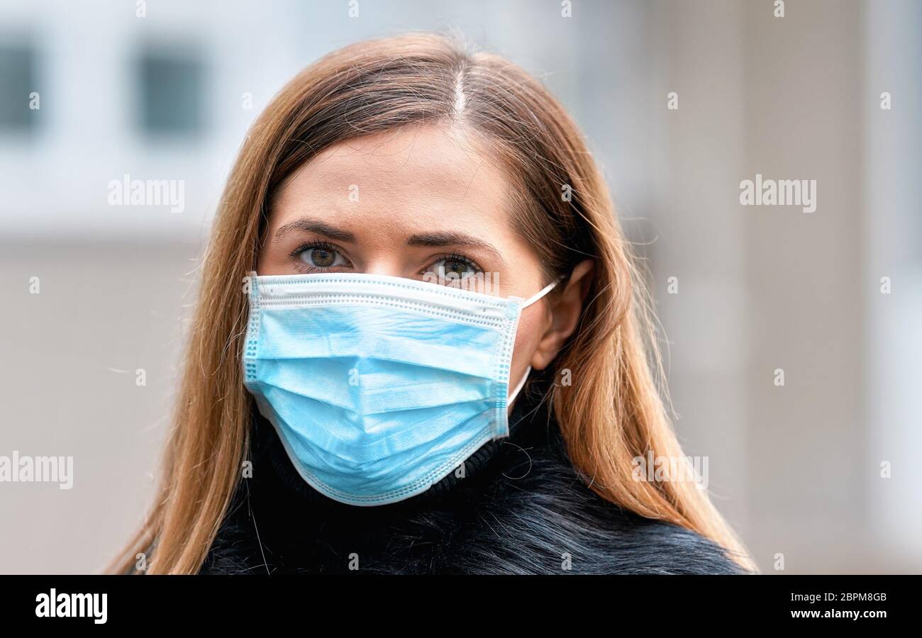 Mujer joven con mascarilla desechable de cara azul virus boca nariz, primer plano retrato. Coronavirus covid-19 concepto de prevención de brotes Foto de stock