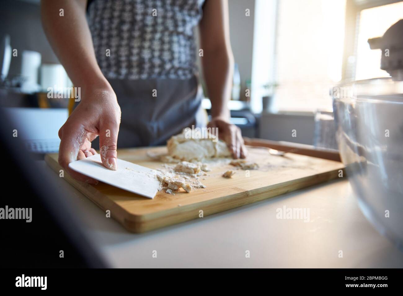 Mujer usando un raspador de masa, haciendo masa fresca en casa en su cocina. Foto de stock