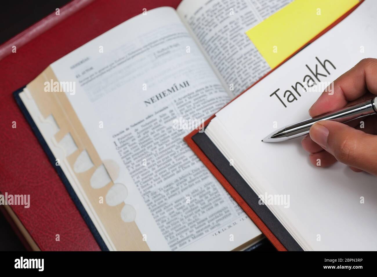 Un estudiante de Tanakh escribiendo en un cuaderno con una biblia abierta al libro del profeta Nehemías. Foto de stock