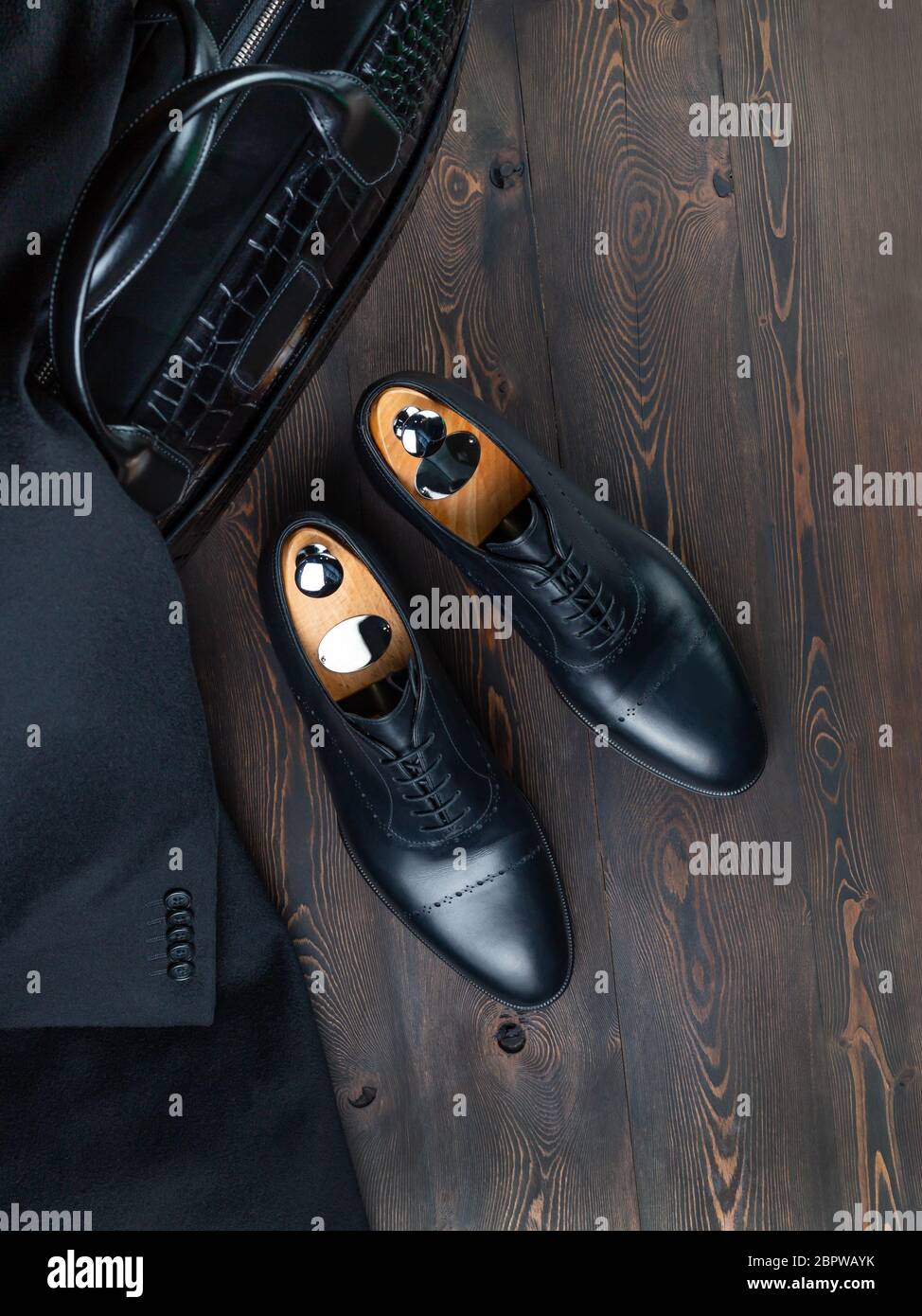 Un par de zapatos negros para hombre sobre bloques de madera en una  superficie de madera junto a un maletín de cuero negro. Moda italiana.  Estilo de saliente Fotografía de stock 