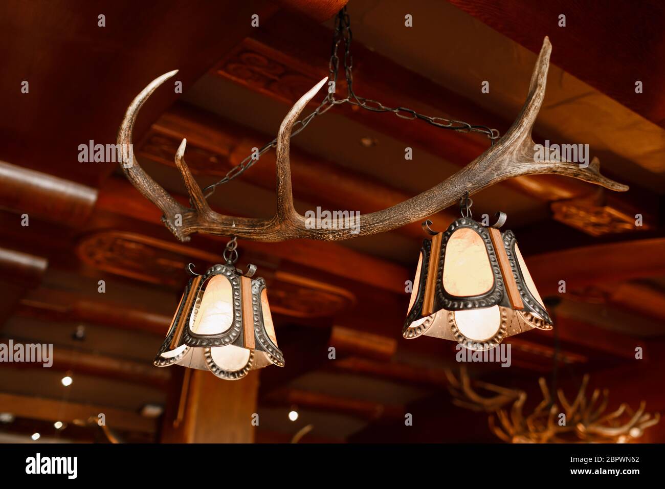 Cerca de una lámpara de araña inusual hecha de cuernos de ciervo o de  cuernos colgando en el interior de la casa o del hotel, no hay gente.  Colores beige marrón. La