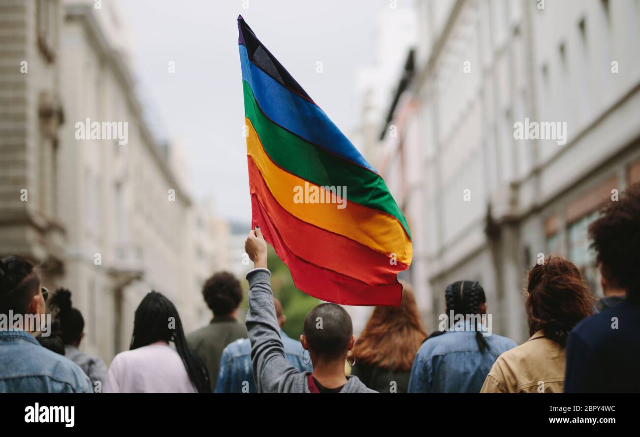 Vista trasera de la gente en el desfile de orgullo. Grupo de personas en la calle de la ciudad con bandera gay arco iris. Foto de stock