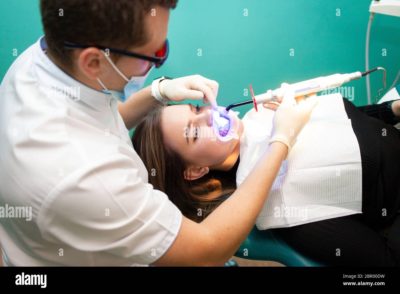 Dentista usando una lámpara ultravioleta blanqueadora en sus dientes. La niña de la clínica