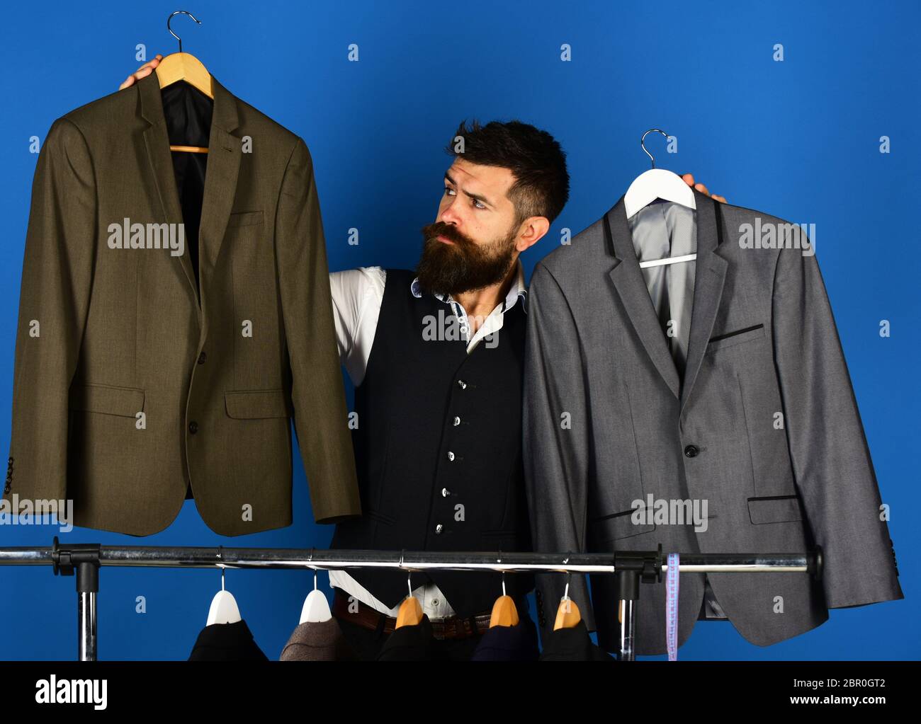 Trajes para hombre con estilo. Ropa masculina en boutique de compras. Hombre  con barba elige trajes clásicos de lujo para hombre cerca de rack en una  elegante sala de exposición. Sastre hombre