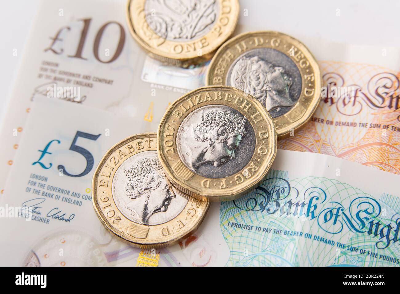 Una libra de moneda con la cara de la reina Isabel II y 5 y 10 libras de billetes en el fondo Foto de stock