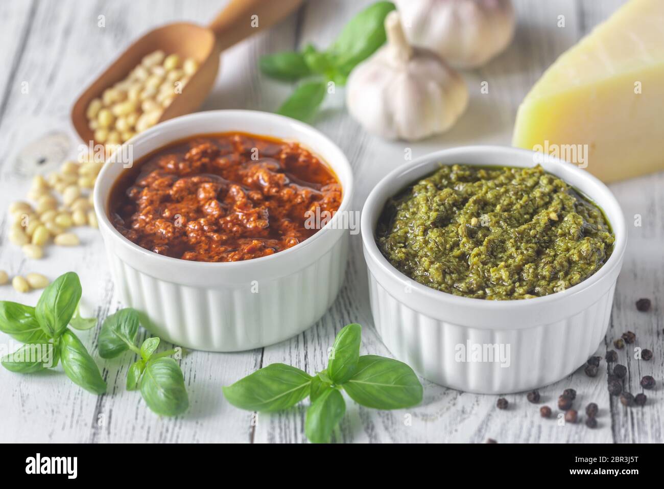 Cuencos de clásico y pesto de tomates secados al sol con ingredientes sobre el fondo blanco de madera Foto de stock