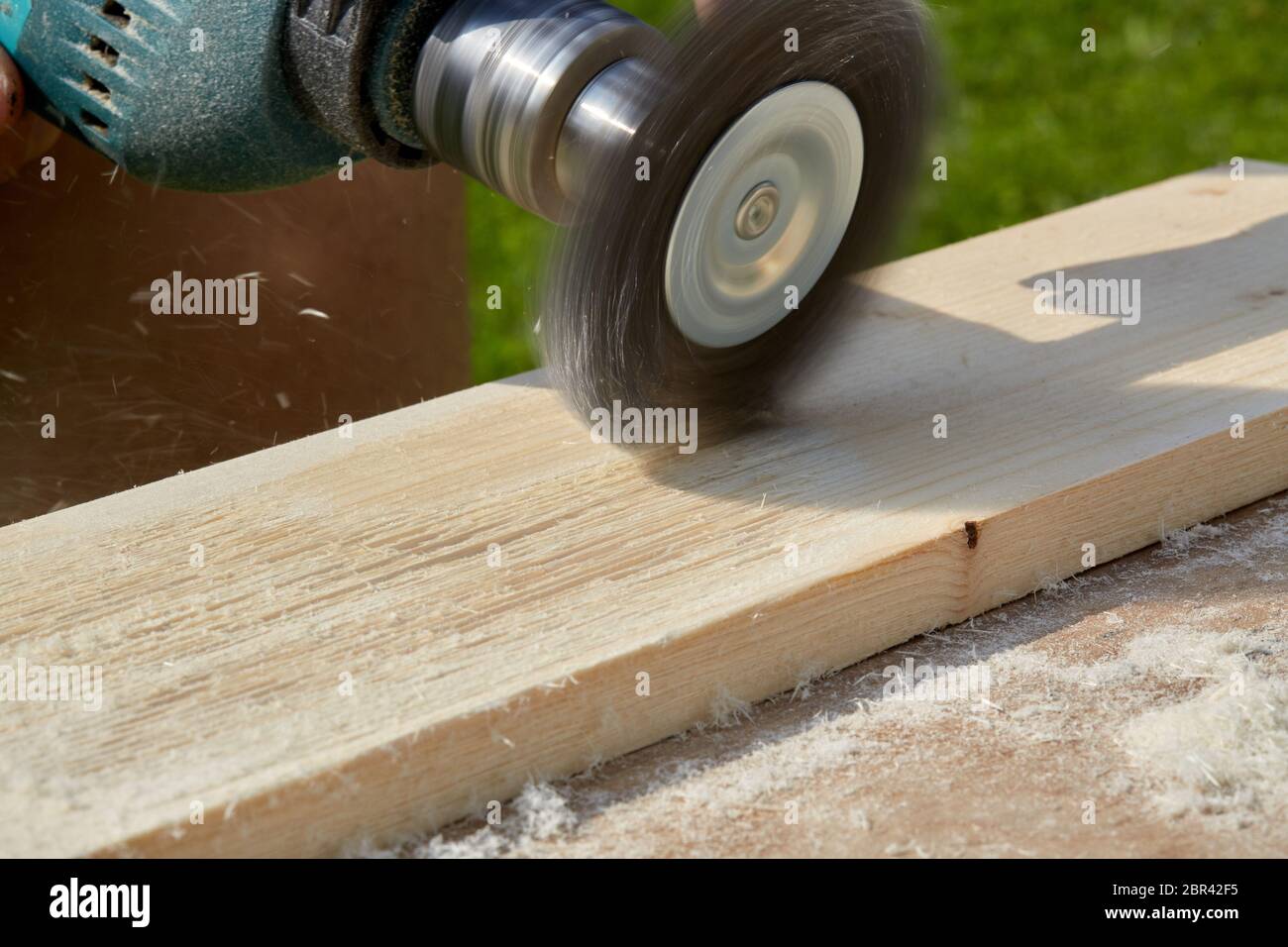 El proceso de cepillado de la plancha de madera. La mano macho sostiene la  máquina de cepillado con rotación eléctrica con disco de metal de cepillo  que lija un pedazo de madera