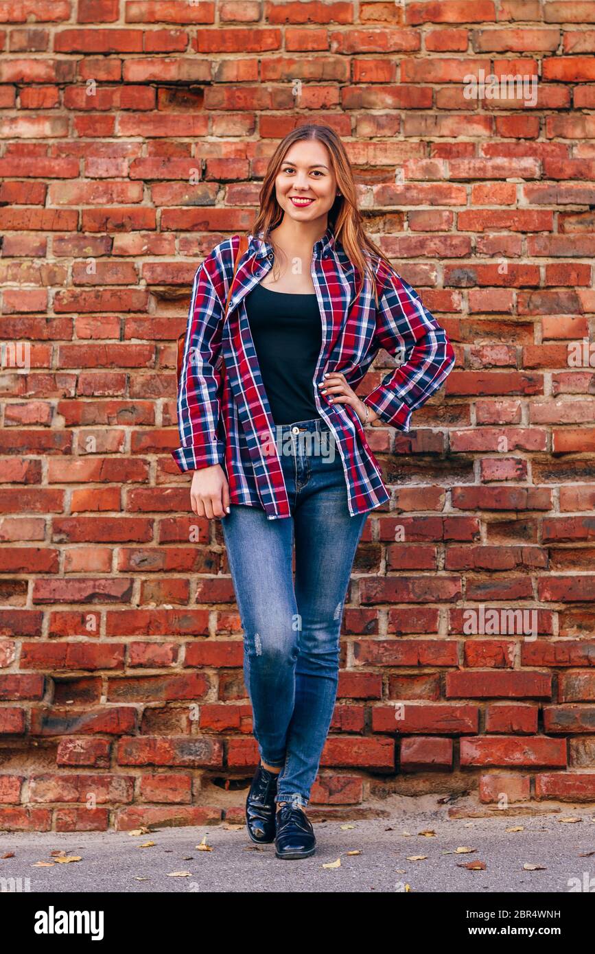 Retrato de mujer joven en camisa a cuadros y jeans de pie contra ladrillo rojo Fotografía de stock - Alamy