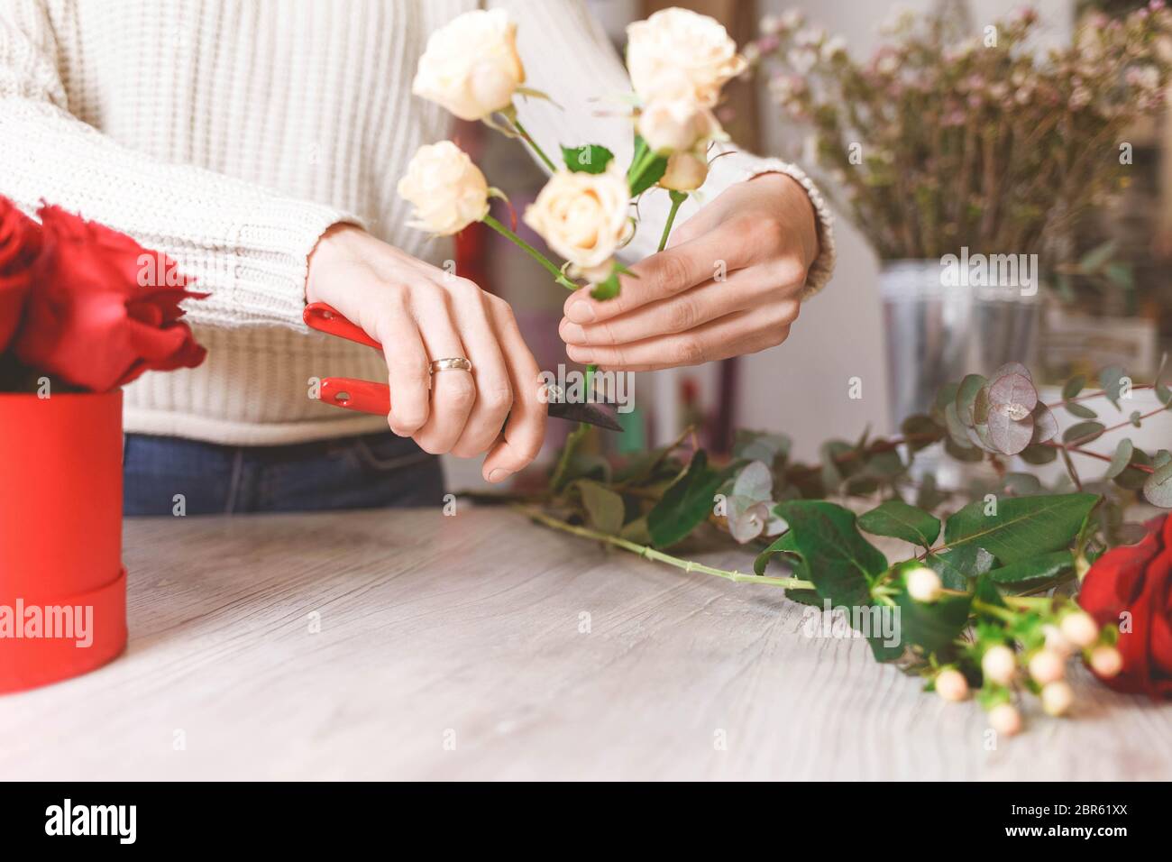 El vendedor de la tienda de flores prepara rosas para crear un ramo podándolas con podas Foto de stock