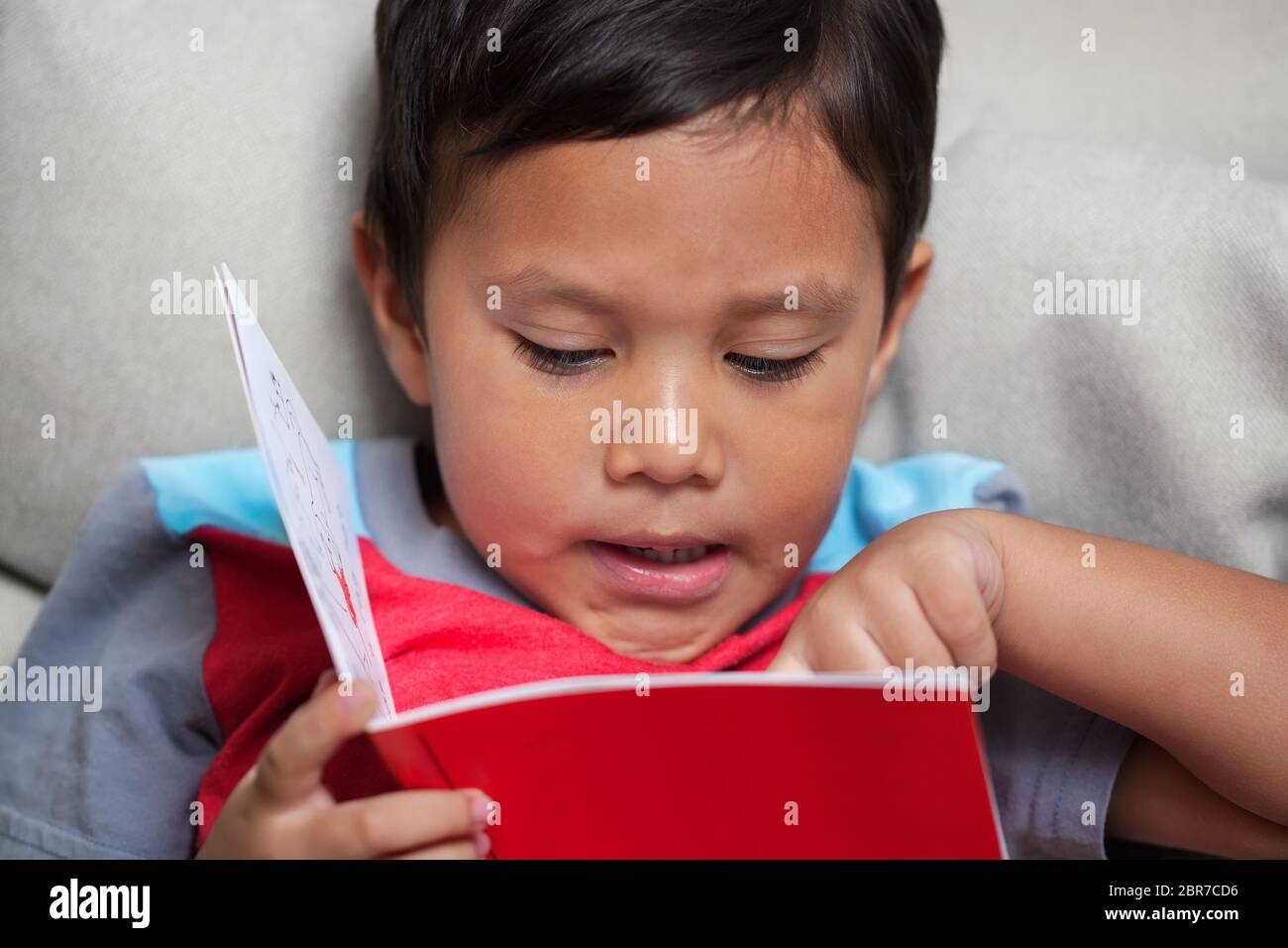 Un preschooler que pronuncia fonética simple está leyendo de un libro de cuentos de estilo lector temprano. Foto de stock